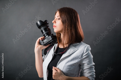 Woman photographer with a SLR camera in her hands posing on a gray background. © Михаил Гута