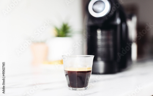 A glass of espresso, black coffee machine on a marble table, white kitchen 