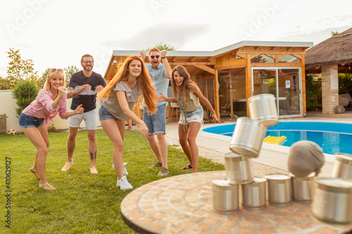 Man throwing a ball knocking down pyramid of tin cans while at a party