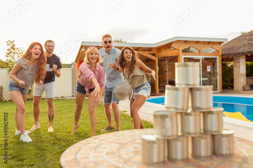 Friends knocking down pyramid of tin cans by throwing a ball at summertime party
