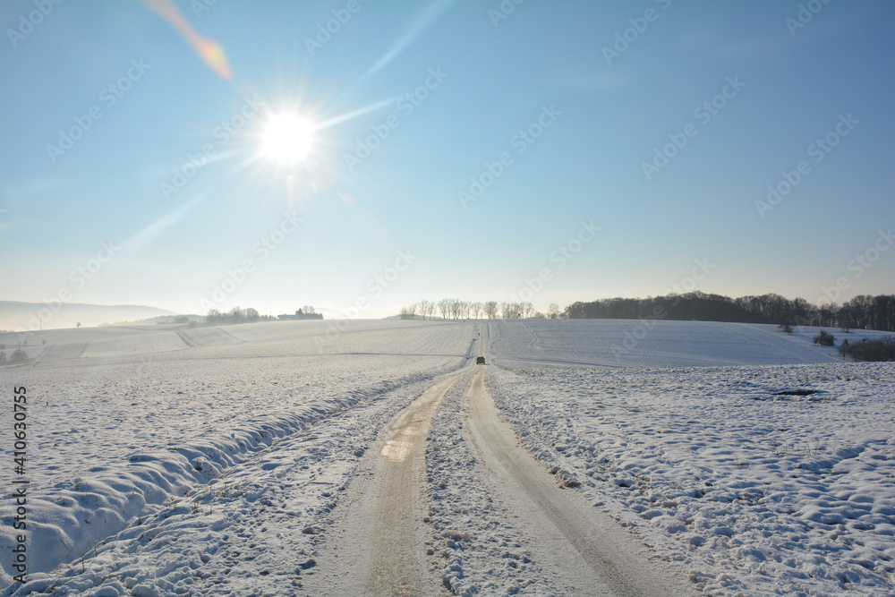 Snow-covered road in the country, with a moving car, a lot of snow in the fields