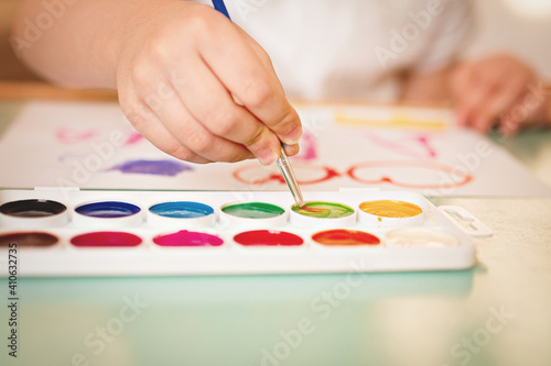 children's hand art brush in paint with palette of watercolors slective focus, film noise