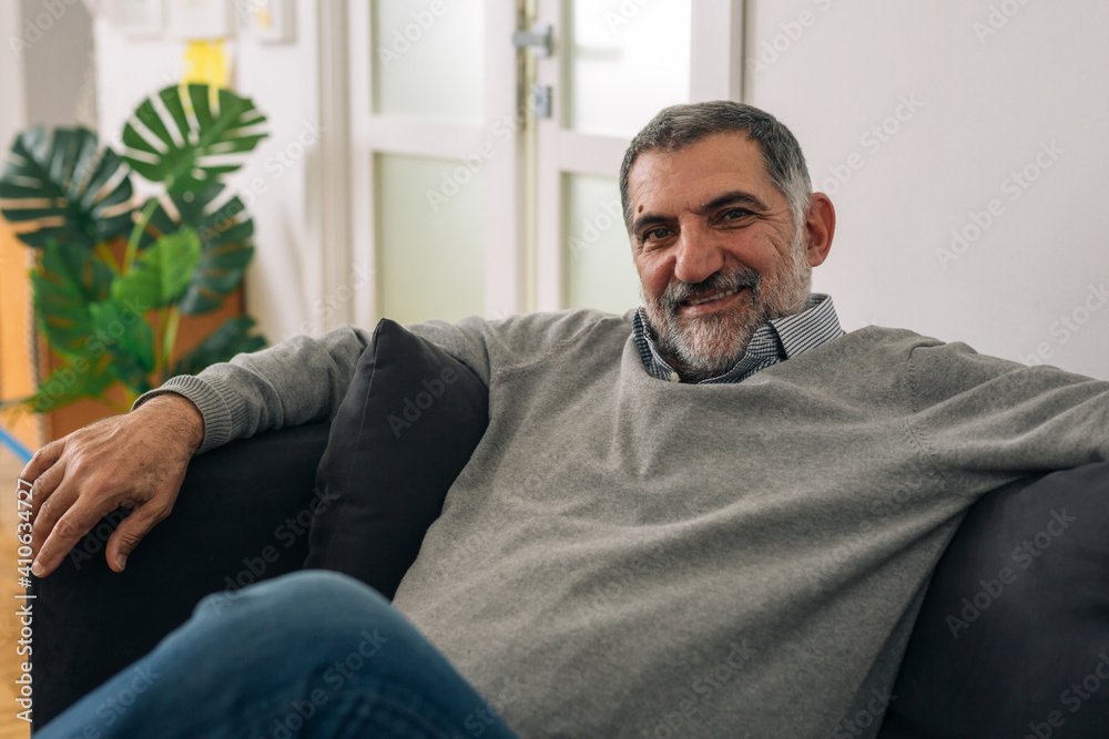positive smiling bearded man sitting on sofa at his home and looking at camera