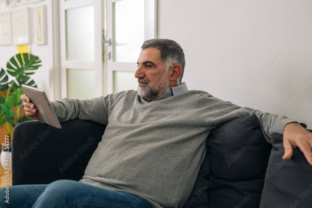 man sitting on sofa in his home and using digital tablet man sitting on sofa in his home and using digital tablet