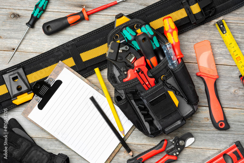 Electrician's tools on the table. An laser tape measure, screwdrivers, tongs, construction tape measure, and a level are spread out on the table. Electrician's bag with tools on the table. Top view