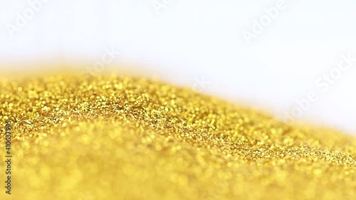 Scattering of shimmery fine round gold glitter on a white surface in close-up. Pouring a strip of sparkling sparkling gold glitter onto the surface with copy space.