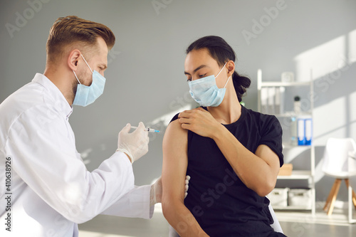 Asian man patient in face mask sitting and getting injection of vaccination for protection from 19-ncov infection from doctor in clinic. Vaccinating against COVID-19 infection during pandemic concept