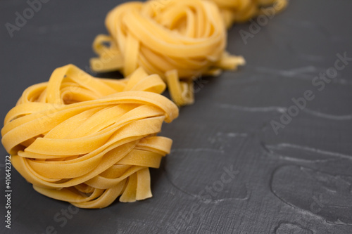 Row of homemade tagliatelle nests, yellow pasta over gray stone background with copy space. Italian food in colors of the year 2021. Fresh homemade or semi finished food, selective focus