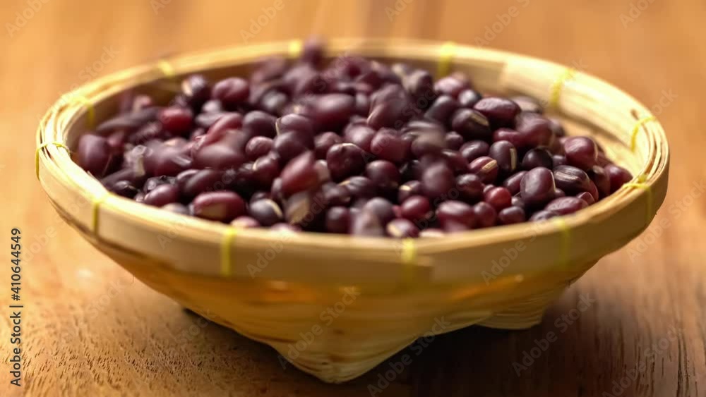 Red beans are falling into bamboo basket on wooden table. Closeup scene of dry adzuki beans falling in a basket. Red beans are falling into bamboo basket on wooden table. Closeup scene of dry adzuki beans falling in a basket.