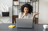 Surprised African-American female freelancer office worker with Afro hairstyle sitting at the desk, with the laptop, working from home office, cannot believe her eyes, received unexpected news online