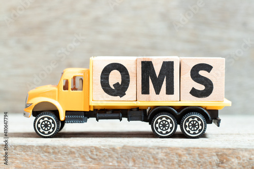 Toy truck hold alphabet letter block in word QMS (abbreviation of quality management system) on wood background photo