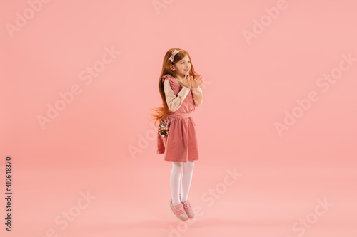 Crazy happy, astonished. Childhood, dream about big and famous future. Pretty longhair girl on coral studio background. Childhood, dreams, imagination, education, facial expression, emotions concept.