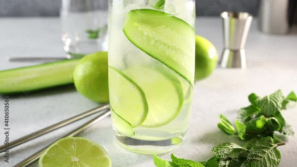 Preparing mojito cocktail or detox cocktail of mint, cucumber and lime in highball glass on a gray concrete stone surface background. Camera moving along glass.