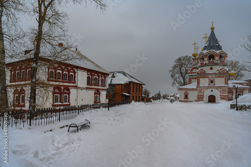 Winter cityscape with a majestic old church, the historic governor's house, a bench in the snow and tall trees. Center of the city of Solikamsk (Northern Ural, Russia) in a winter cloudy day 