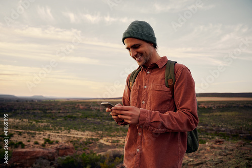 Φωτογραφία Happy male hiker with backpack and cap using smartphone on mountain