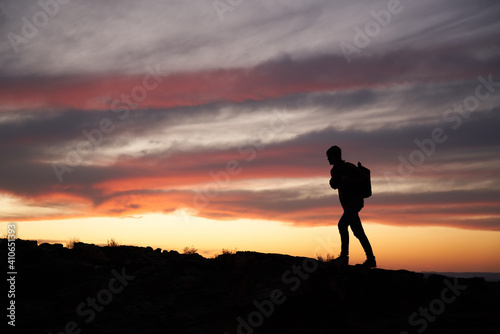 Silhouette of a male traveller with a backpack climbing up the mountain against beautiful sky