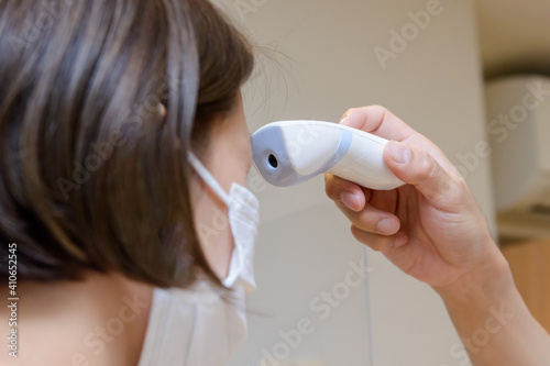 検温　非接触型の体温計を女性のおでこにあてるシーン photo