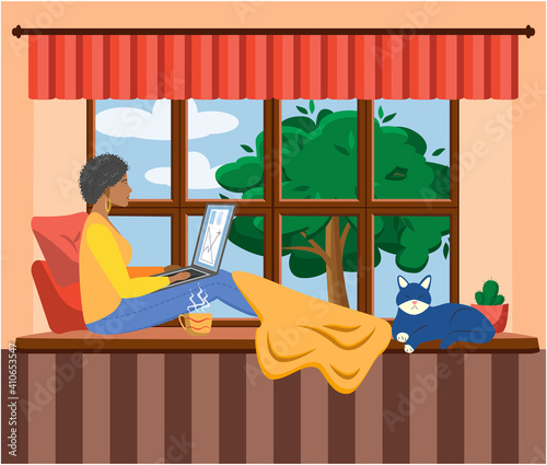 A woman works at a laptop while sitting on the windowsill at home. Freelance concept, quarantine due to covid-19.