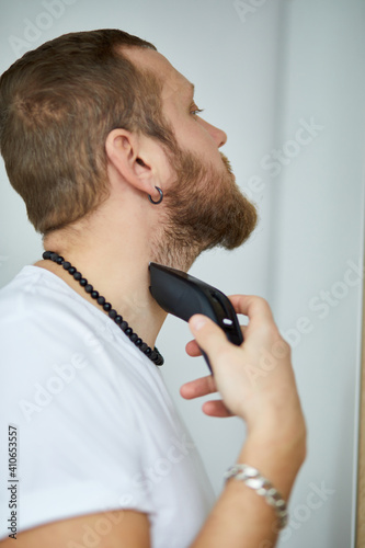 Handsome man in white t-shirts cutting beard, moustache personally himself with trimmer