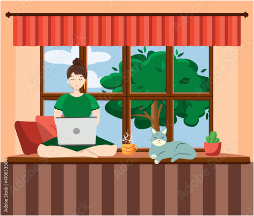 A woman works at a laptop while sitting on the windowsill at home. Freelance concept, quarantine due to covid-19.