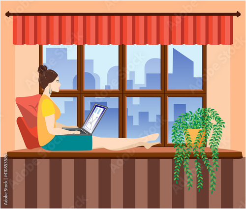 A woman works at a laptop while sitting on the windowsill at home. Freelance concept, quarantine due to covid-19.