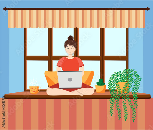 A woman works at a laptop while sitting on the windowsill at home. Freelance concept, quarantine due to covid-19.