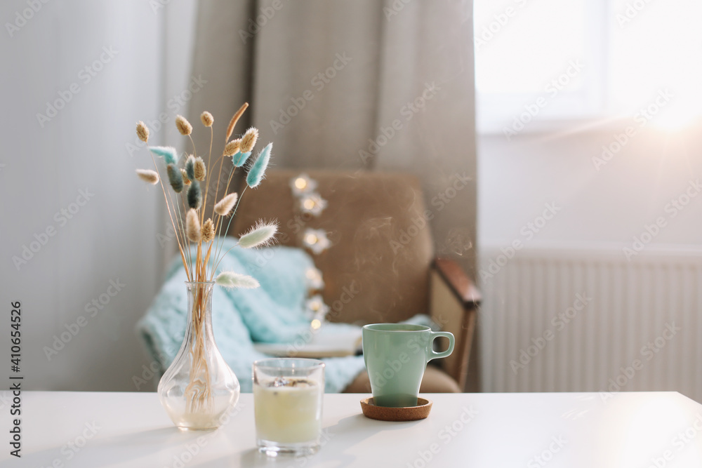 Lifestyle composition with cup of coffee, candle and a vase with flowers on a coffee table. Cozy home interior decoration concept