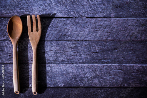A couple of wooden utensil, a spoon and a carving fork, laid on a dark wooden table with copy space on the right side