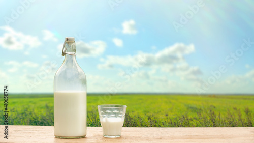 Bottle and glass with fresh milk on a background of green meadow and blue sky photo