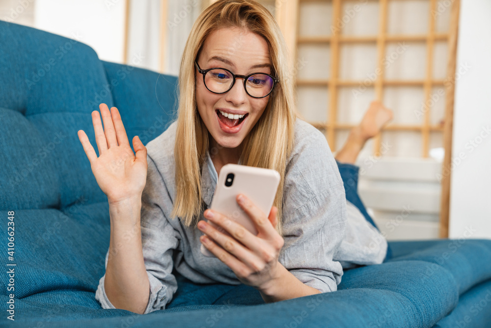 Excited woman waving hand and using cellphone while lying on couch Excited woman waving hand and using cellphone while lying on couch