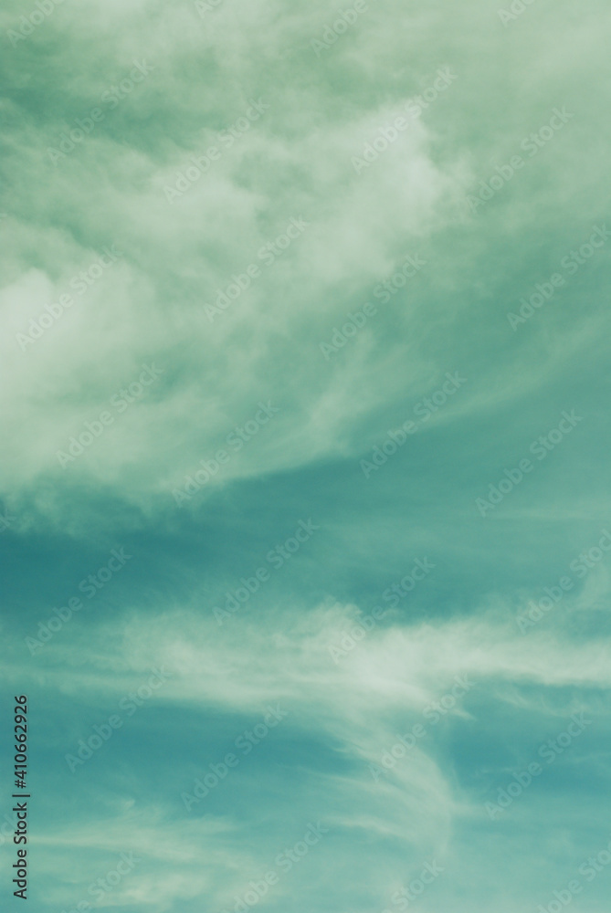 Fototapeta premium Colorful blue green sky with dramatic soft light clouds. Vertical capture natural image background.