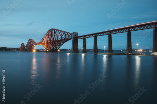 View of Forth Rail Bridge at night and and the glow trail of a moving train over the sea. View of Forth Rail Bridge, the worlds longest cantilever bridge, Scotland, United Kingdom