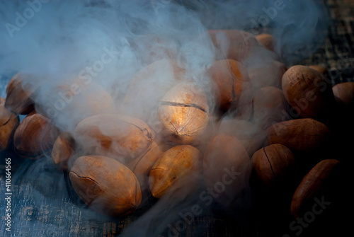 Pecan texture close up. Nuts on a pile on a black wooden board. Contrasting dramatic light as an artistic effect. Nuts in blue smoke.