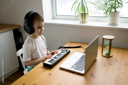 Preschooler boy in headphones learns to play the musical keyboard online. Distance learning to play the piano. Online music lessons