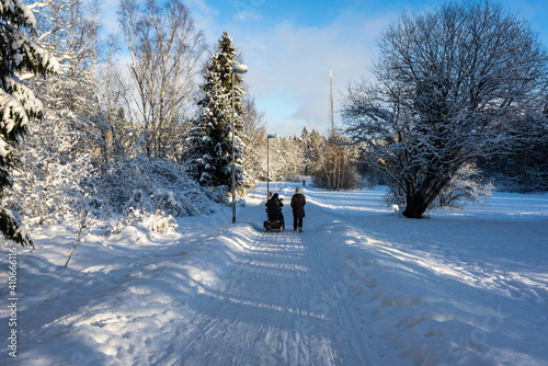 People with disabilities on a walk. Barrier free environment for wheelchair users. Assistant walks in the winter forest with his ward. Beautiful winter snowy road in woods. Trees pines firs. Blue sky.