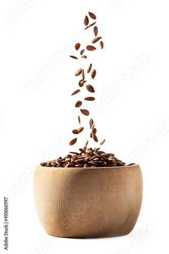 Side view of small wooden bowl filling with linseed or flax seed falling down and isolated on white background