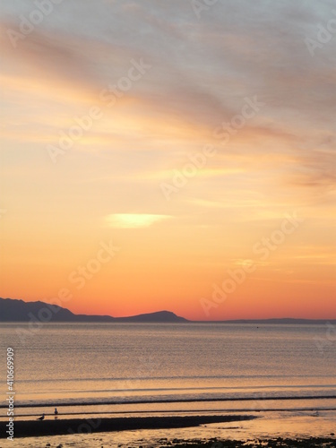 Sunset over the Firth of Clyde taken from Prestwick beach, with north end of Arran silhouetted against the sunset sky and figures at the water's edge © Alistair MacLean