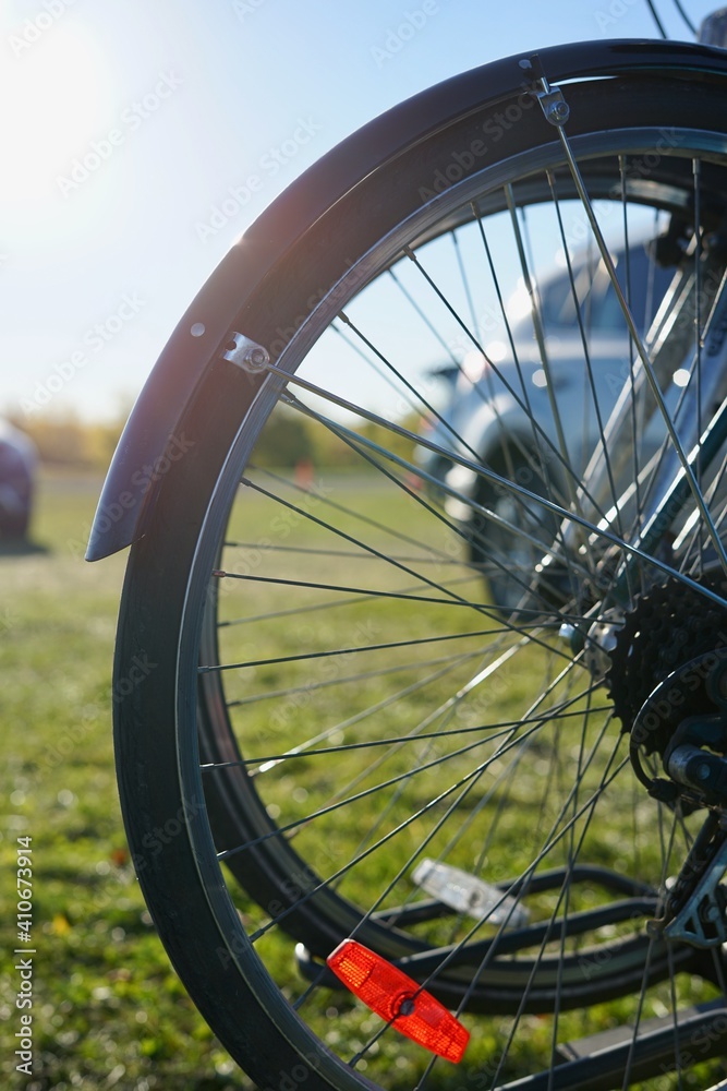 Part of a bicycle wheel with spokes on the background of cars and the blue sky. Part of a bicycle wheel with spokes on the background of cars and the blue sky.