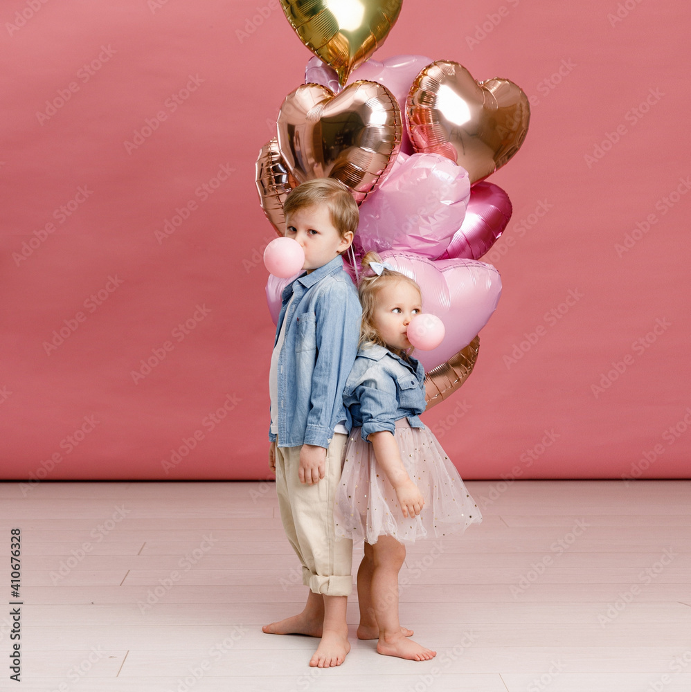 Little boy and girl hugging, dancing, smiling and having fun near big branch of pink heart-shaped ballons. Valentin’s day concept . Isolated on pink background.
