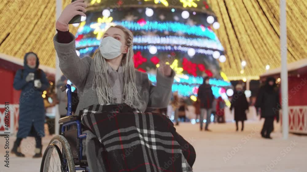 Young woman in a wheelchair at Christmas party on the streets wearing a mask - taking selfie Young woman in a wheelchair at Christmas party on the streets wearing a mask - taking selfie