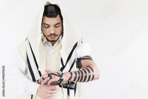 Young Orthodox Jew in shawl (tallit) putting on phylacteries (tefilin) on left arm. photo