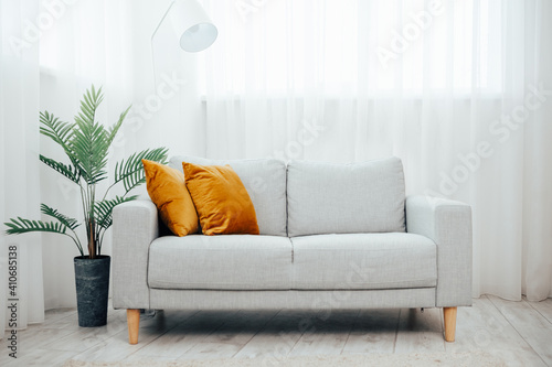 Gray sofa with yellow pillow simple living room. modern living room with cozy sofa and flower in a pot - palm tree, background large light windows and curtains            