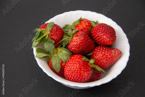 fresh large garden strawberries lie in a white bowl on a dark background