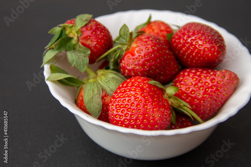 fresh large garden strawberries lie in a white bowl on a dark background