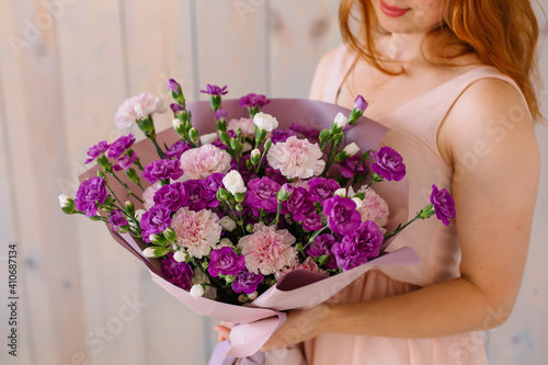 Bouquet of Violet-pink carnations and Shabo carnations in female hands on a wooden background Woman in a pink festive dress