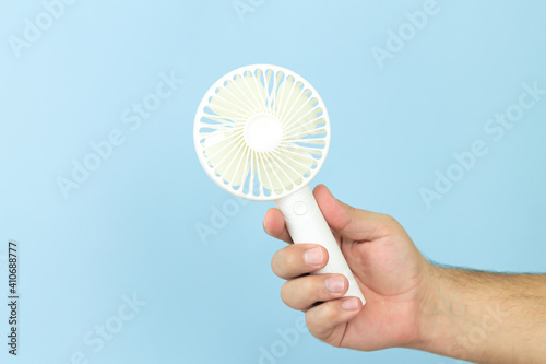 Man holding small portable usb fan close-up isolated on blue background