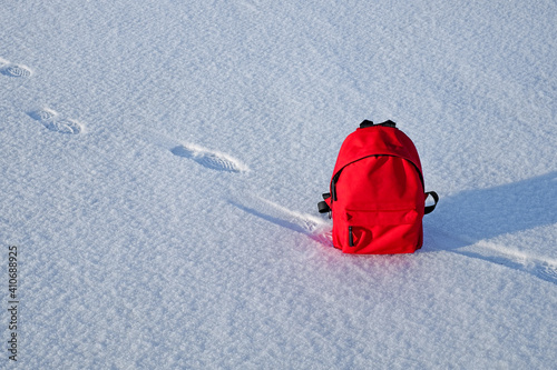 Red packbag and human footprints in snow and blue winter sky. Copy space. photo