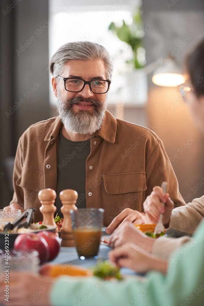 Mature bearded man sitting at dining table during lunch with his family Mature bearded man sitting at dining table during lunch with his family