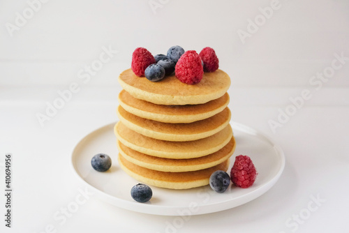 Freshly cooked soft delicious gluten free pancakes stacked on white plate, served with fresh berries, close up. Space for text. Healthy sweet food.