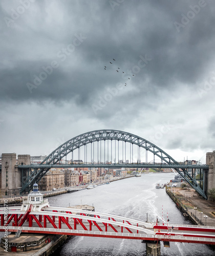 The Newcastle upon Tyne North East Quayside and swing bridge with river passing below vertical panorama to show cityscape and stunning dramatic thunder clouds with birds flying in sky photo